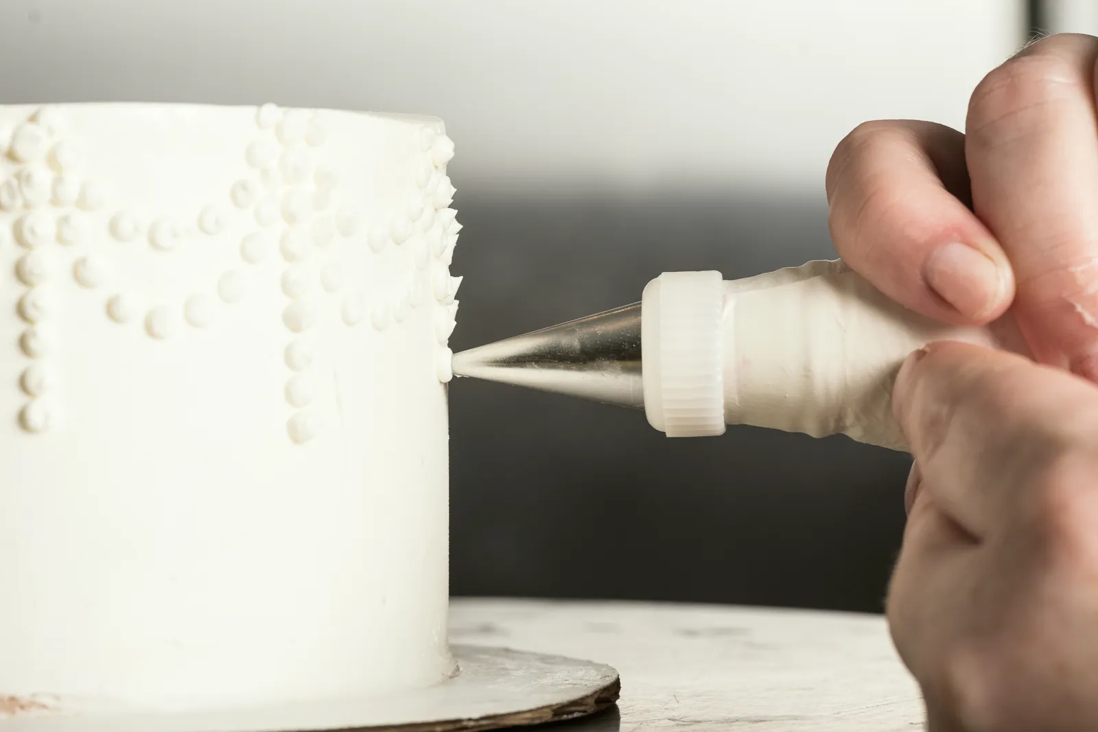 Hands piping small white dots onto a wedding cake.