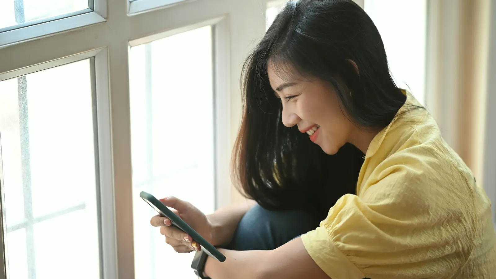 A client booking an appointment on her phone by a bright window.